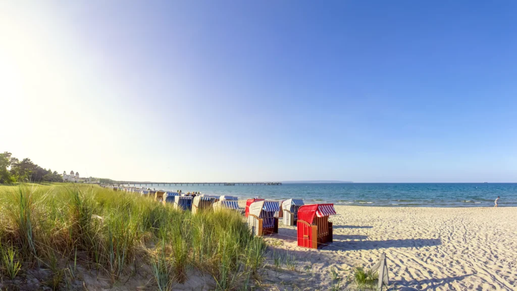 Dein perfekter Ausflug zum Hundestrand Binz 8 Sonniger Strand mit Pier, Strandkörben und Restaurant in Binz an der Ostsee, Menschen genießen Meer und Sand.