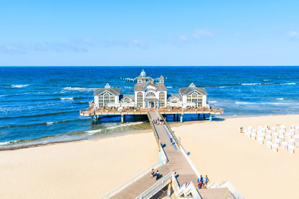 Dein perfekter Ausflug zum Hundestrand Binz 4 Sonniger Strand mit Pier, Strandkörben und Restaurant in Binz an der Ostsee, Menschen genießen Meer und Sand.