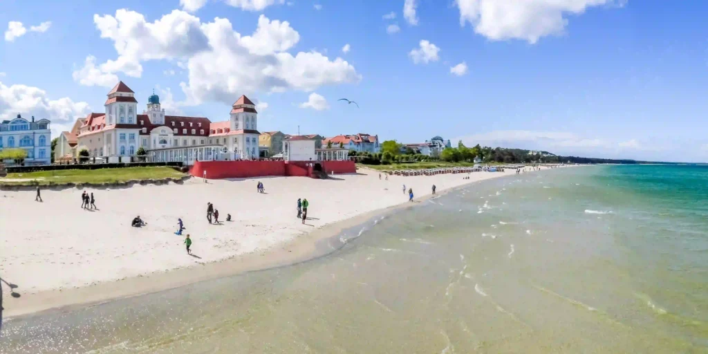 Rügen mit Hund: Perfekter Urlaub für dich & deinen Vierbeiner 4 Weitwinkelaufnahme eines belebten Strandes auf Rügen mit Hund, blauem Himmel, Promenade und Strandkörben am Meer.