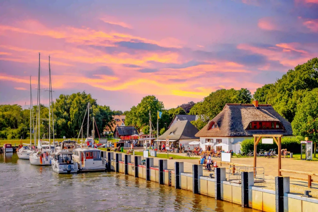 Rügen mit Hund: Perfekter Urlaub für dich & deinen Vierbeiner 7 Sonnenuntergang am Hafen mit Booten, Reetdachhäusern und Menschen – perfektes Motiv für ein Urlaub.