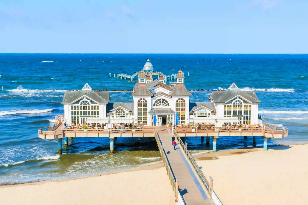 Rügen mit Hund: Perfekter Urlaub für dich & deinen Vierbeiner 5 Großer Pier mit Restaurants am Meer, heller Sandstrand und blauem Himmel – perfektes Ziel für Rügen mit Hund Urlaub.