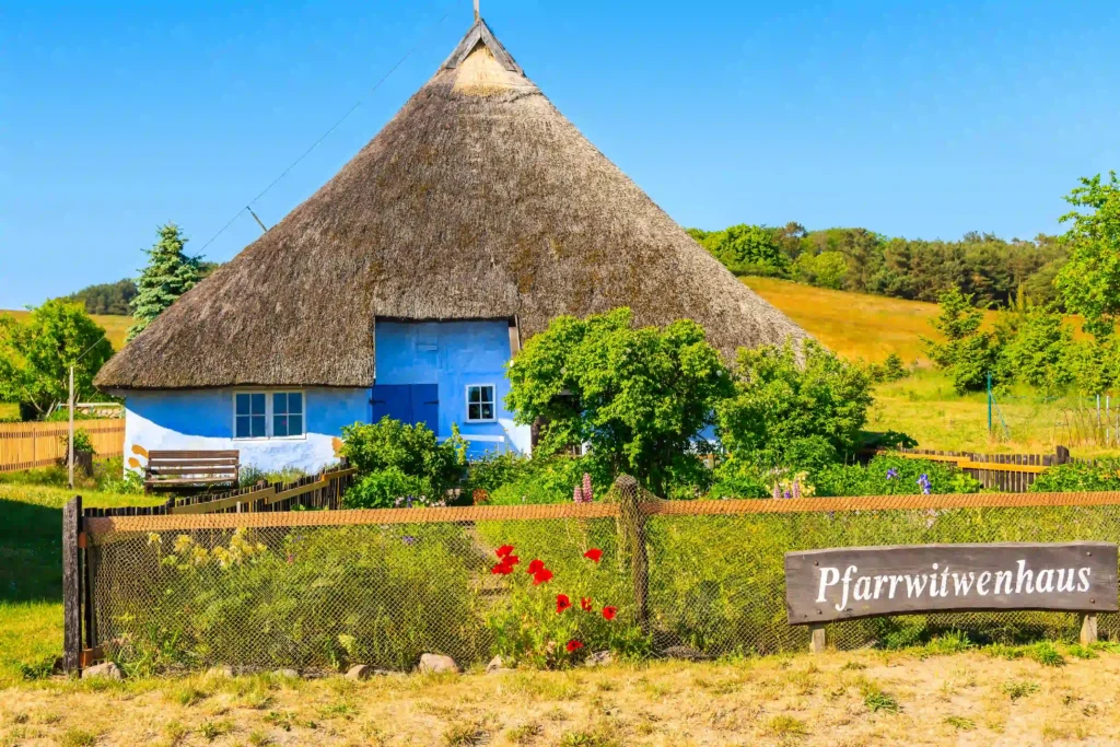 Rügen mit Hund: Perfekter Urlaub für dich & deinen Vierbeiner 17 Traditionelles blaues Haus mit Reetdach und Garten auf Rügen mit Hund an sonnigem Tag und klarem Himmel.