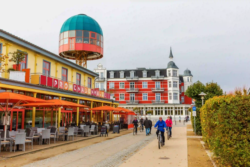 Urlaub mit Hund in Zinnowitz: Dein perfekter Ostseeurlaub 9 Lebhafte Promenade in Zinnowitz mit Hund, Fahrradfahrern, Cafés und markanter Architektur unter bewölktem Himmel im Herbst